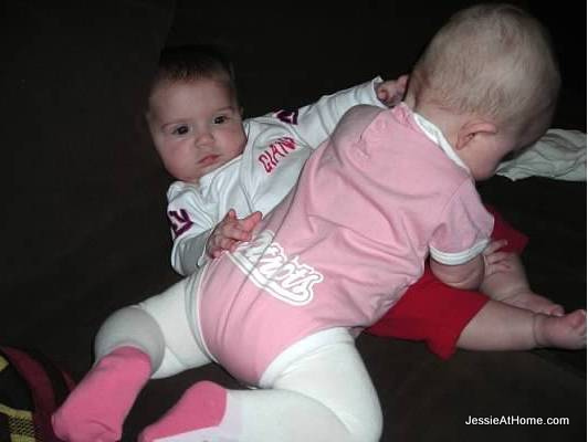 Vero in Patriots Onesie laying over top of Kyla in Giants top.