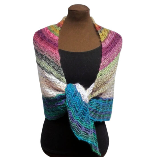 Front of a brown dress form in a black tank top with a triangular crochet shawl with stripes of varying sizes in shades of cream, pink, green, and blue. The shawl sides are pulled over the shoulders and around the body with the two end points tied at the waist.