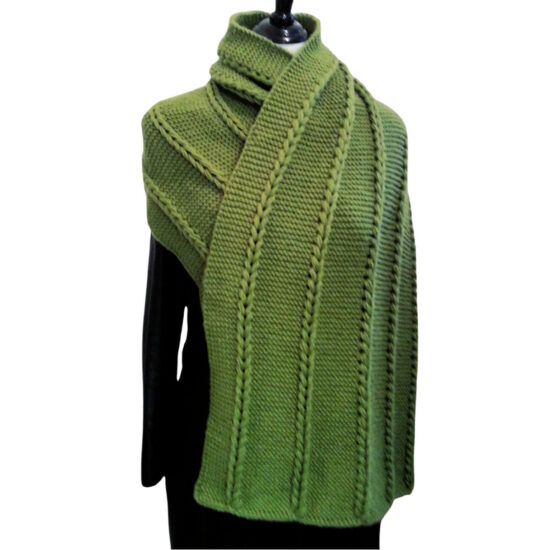 A dress form in a black leather coat with a rectangular shawl draped over the shoulders with one side tucked under the other. The yarn is grass green and knit in the garter stitch with 5 vertical sections of chunky chains made with several strands of yarn in each chain.