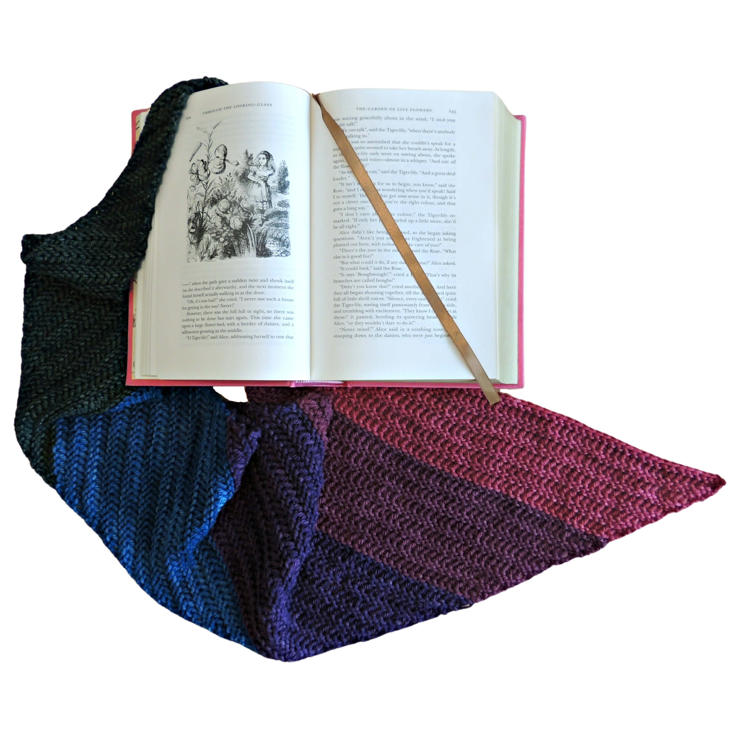 Flat lay overhead of a hardcover of "Alice's Adventures In Wonderland" opened to a page with an image with a gold ribbon bookmark across it. Loosely gathered around the book is a long skinny triangular wrap in stripes starting at the point with green, blue, purple, wine, and lastly red. The stripes get thinner as they move away from the point.