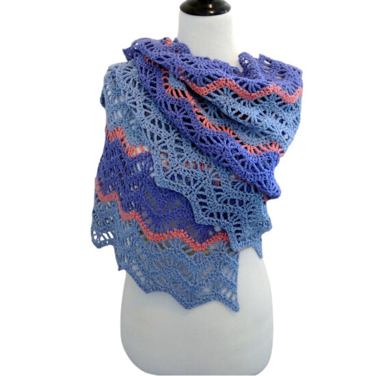 Off-white dress form in a lightweight chevron crochet wrap with alternating rows of solid stitches and lacy open stitches which accentuate the chevrons. The wrap is made with thick strips of light and medium blue yarn separated by thin stripes of coral yarn. The wrap is wrapped around the shoulders and torso of the dress form with the top end tossed from front to back over one shoulder.