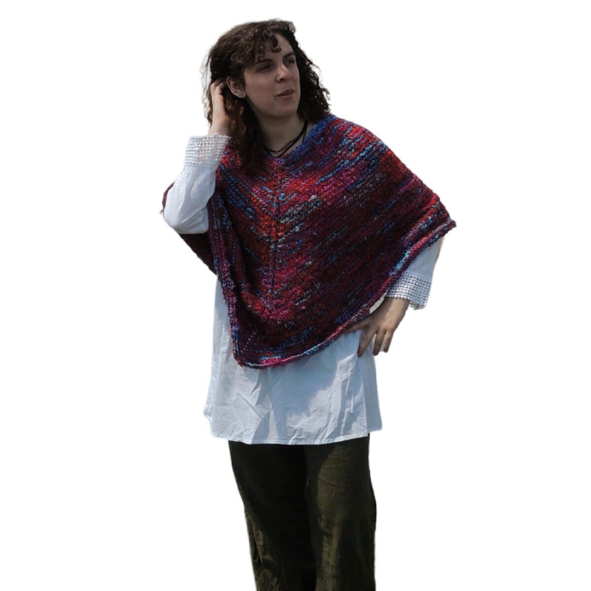 Front view of a young woman with curly hair wearing a white blouse, black pants and a classic poncho with points in the front and back. The poncho is knit with yarn that's mostly scarlet with short lines of blues and pinks. She has one hand on her hip and the other on the side of her head.
