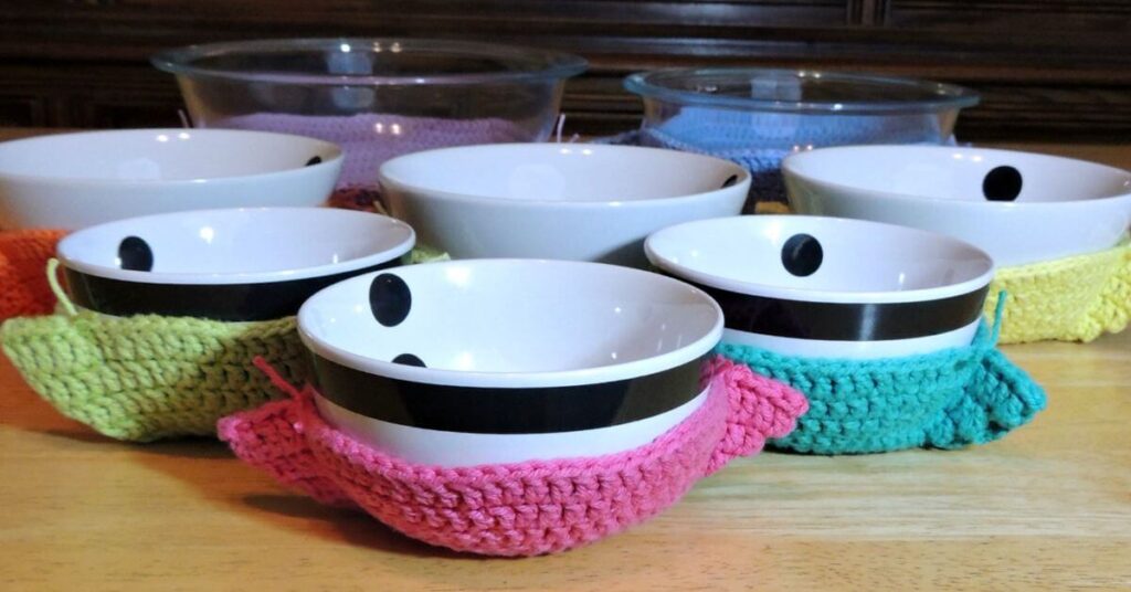 Image of several bowls in crochet bowl cozies of various colors.