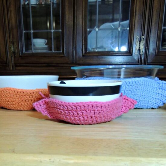 Image of several bowls in crochet bowl cozies of various colors.