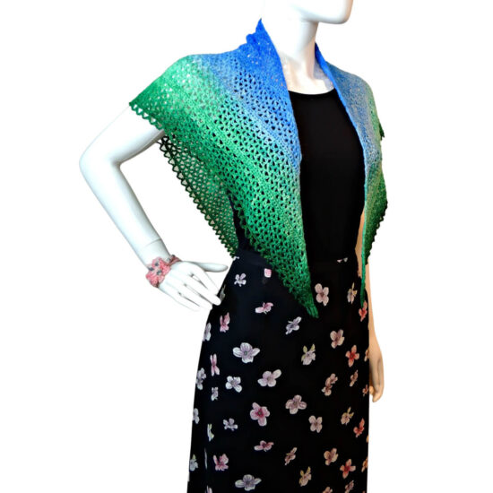Waist up of a mannequin in a black tank top and skirt with a triangular crochet lace shawl with a scalloped chain edge draped over its shoulders. The shawl changes color from the top center out from dark blue to light blue to light green to dark green.