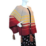 Side front view of a white mannequin in a black skirt and an open front poncho that's essentially a square with a slit in the from the center of one side to the center of the square. The slit is in the center front. The poncho is crocheted in yarn starting in tan, then changing in stripes to yellow, rust, then burgundy. Tassels hang off the points.
