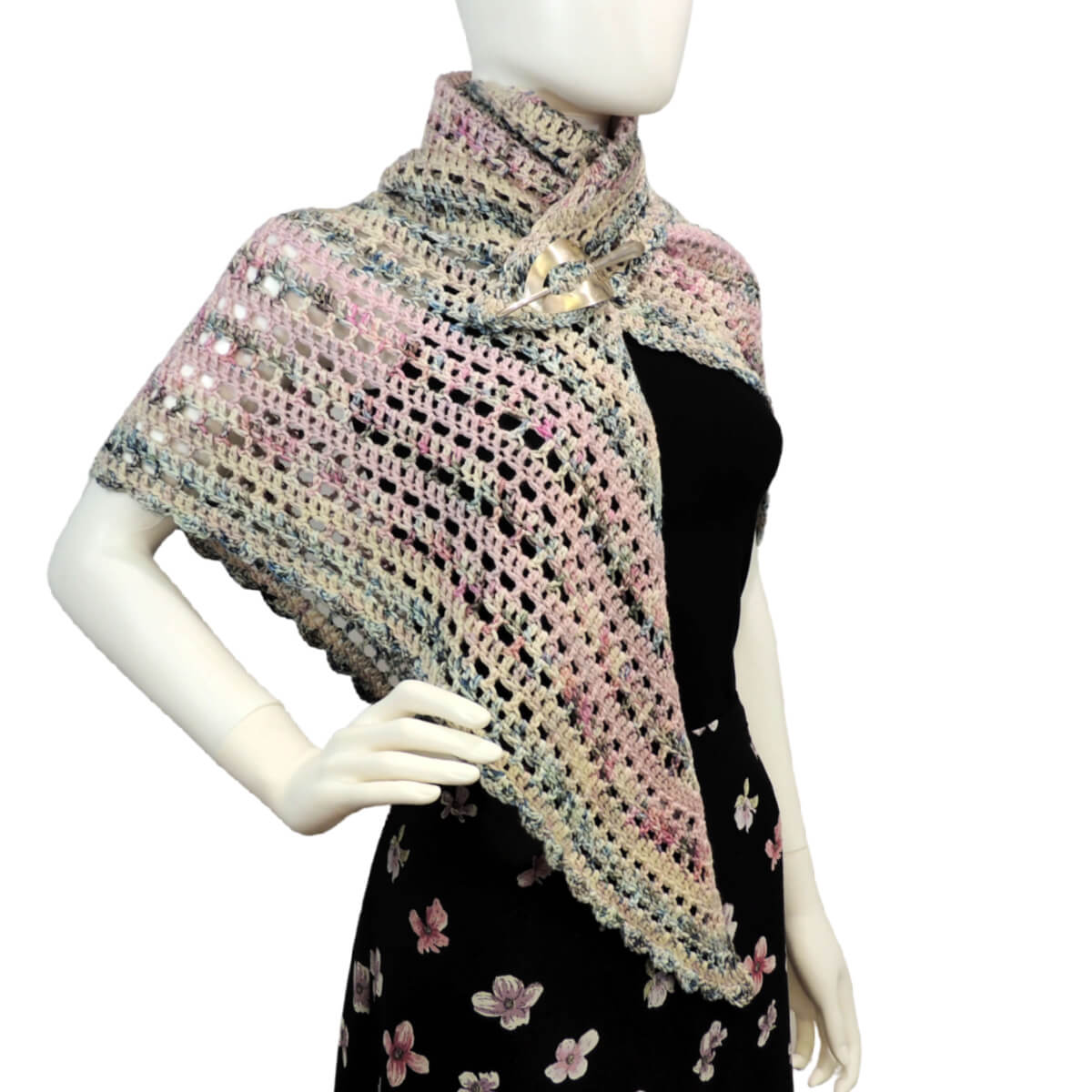 Front angled view of a white mannequin in a black skirt, black tank top, and a triangular shawl that's almost a 45/45/90 triangle, but is slightly off so all 3 sides and angles are different. The shawl is crocheted in alternating rows of solid stitches and mesh stitches in yarn lightly colored in shades of pale pink, pale blue and pale yellow. The 2 shorter of the 3 sides have a scalloped border. One point of the shawl hangs in front so the shawl drapes over the shoulder and is then wrapped around the neck twice and attached to the first side with a silver shawl pin.