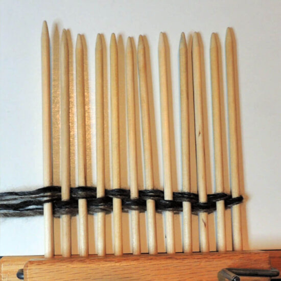 12 pointed wood dowels clamped together in a row with yarn woven through them twice.