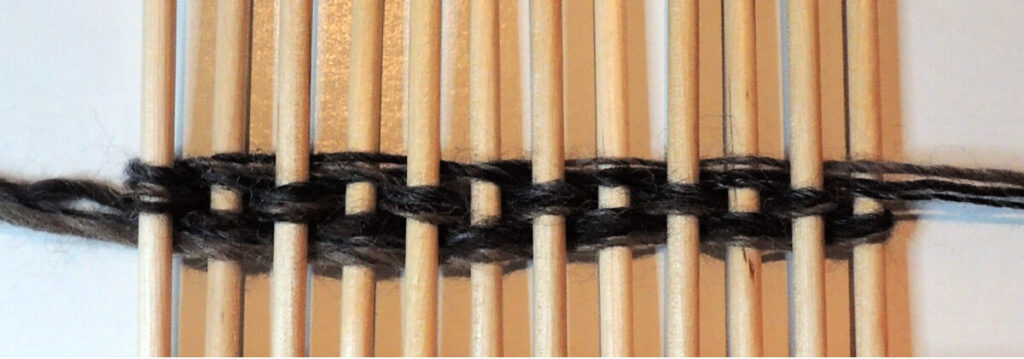 12 pointed wood dowels in a row with yarn woven through them several times.