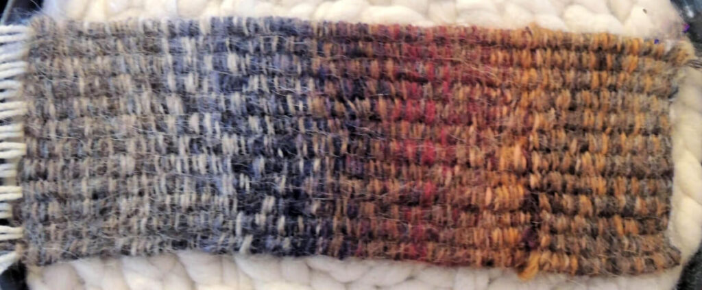 A long, thin piece of weaving that changes color from gray to blue to brown.