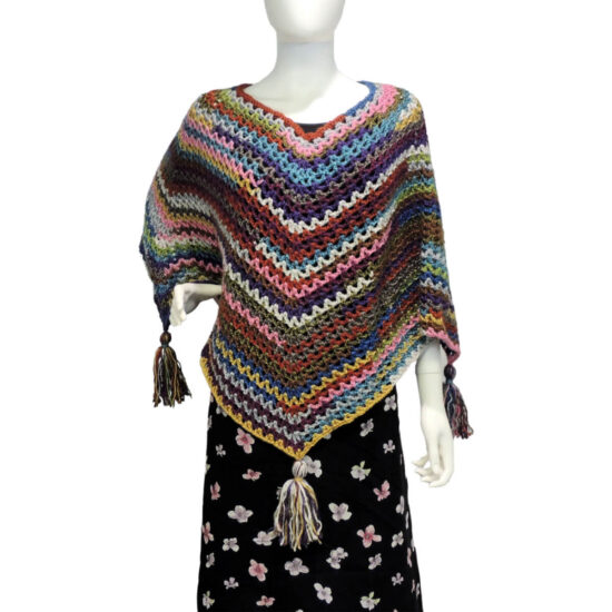 Front of a mannequin wearing a black skirt and a multicolor V-stitch crochet square poncho with large tassels hanging from each of the 4 points.