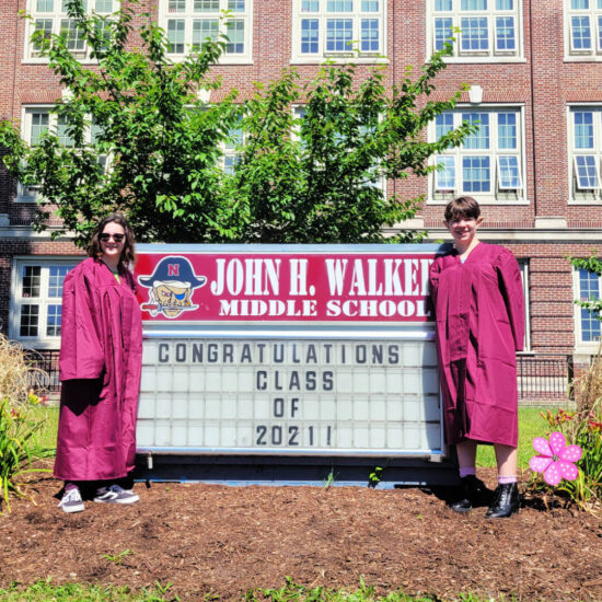 Two kids in maroon robes standing in front of an eighth grade graduation sign.