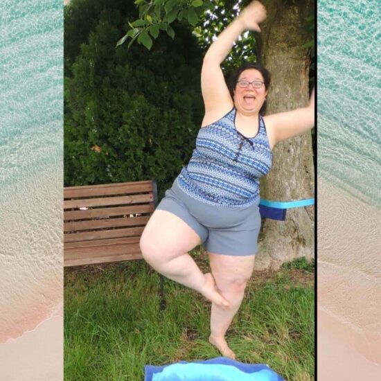 Image of a woman (Jessie) outside in front of a bench and tree, wearing a blue and gray tankini and starting to fall while trying to do the yoga tree pose.