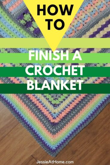 Vertical rectangular photo of the corner of a blanket at a 45 degree angle on a dark wood floor. The blanket is crocheted in light rainbow colors with the final border section made in linen stitch. At the top of the image is a yellow tringle with green stripes below, all under the text "how to finish a crochet blanket." Along the bottom is text "Jessie At Home dot com."