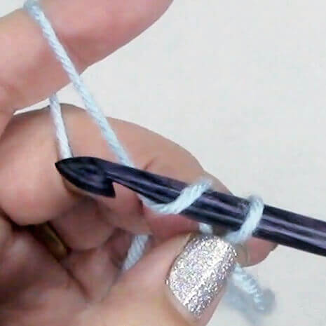 image of a hand making a crochet chain with a crochet hook and blue yarn