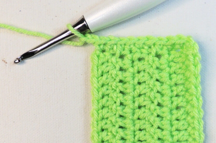 A green rectangular piece of crochet that continues off the bottom of the image. At the top left corner is a crochet hook attached to the unfinished border.
