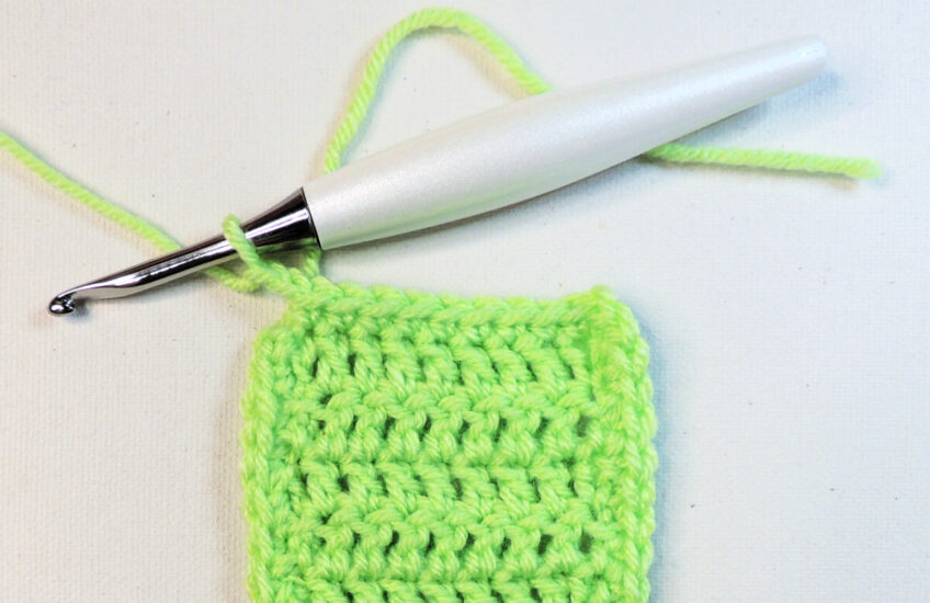 A green rectangular piece of crochet that continues off the bottom of the image. At the top left corner is a crochet hook attached to the last stitch of the border.