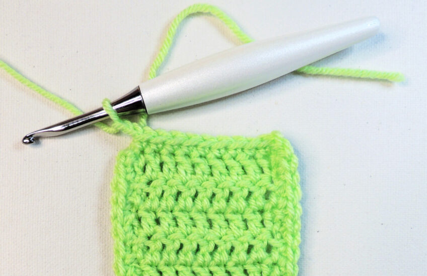 A green rectangular piece of crochet that continues off the bottom of the image. At the top left corner is a crochet hook attached to the last stitch of the border.