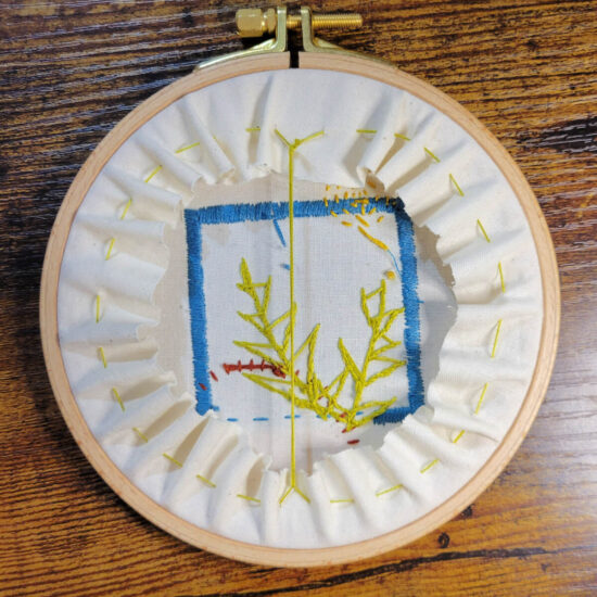 Back of an embroidery hook with off white fabric stretched in it. The back of embroidery is visible inside the hoop. The extra fabric has been cut an even distance from the hoop and is gathered in with a running stitch so it can not be seen from the front.