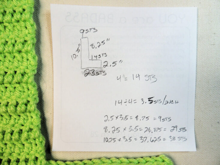 Square piece of paper with measurements and math on it, a green piece of crochet on the side.