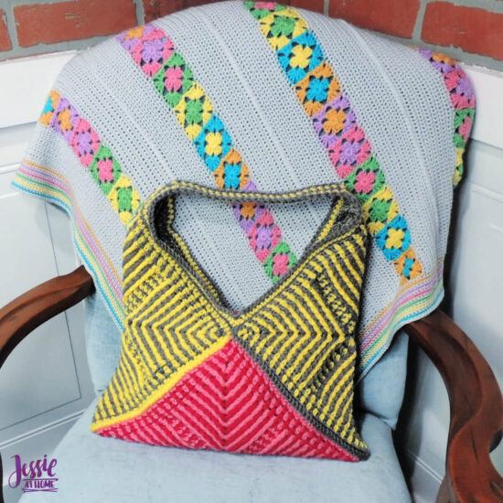 Purse made of three crochet squares folded diagonally. Each has angled stripes pointing in from corners made with post stitches. The bottom is two tone pink and the rest is gray and yellow. Purse is on a light blue chair.