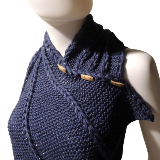 Three quarter front view of the top third of a white mannequin wearing a black tank top and a dark blue knit buttoned cowl that is thin on one end then wraps around the neck and buttons to the other end which has flared out with 5 points. There are columns of raised large stitches from the short end to the tips. The cowl is buttoned on the side facing us.