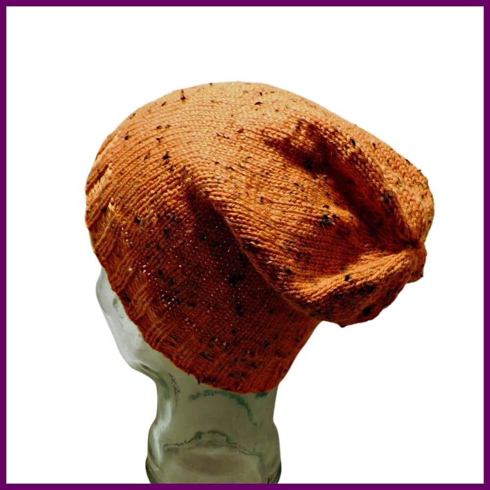 Photo of back side of glass mannequin head in an orange tweed knit stocking hat with rib stitches at bottom and stockinette stitches for rest of hat. Top is gathered to close.