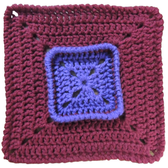Crochet square that starts with purple on the inside, then has a section of burgundy that is attached below the last round of the purple, making the last round stand up.