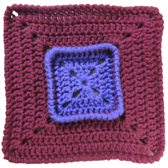 Crochet square that starts with purple on the inside, then has a section of burgundy that is attached below the last round of the purple, making the last round stand up.