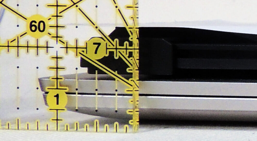 A straight on view of a the corner of a closed laptop with a second screen attached to the back. A ruler has been placed in front of it so that it is clear that the laptop is 5/8 of an inch high and the second screen is another 5/8 of an inch.