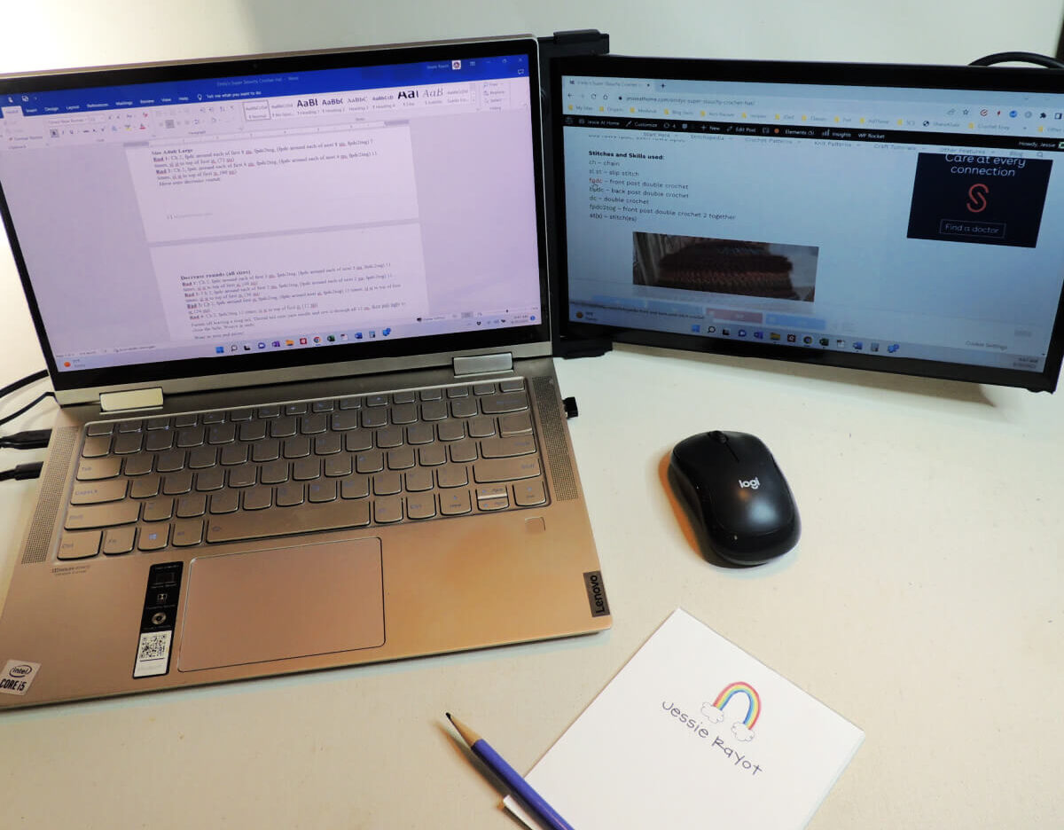 Slightly overhead image of an open laptop with a typed document on the screen, pulled out from behind the laptop and to the right and at a slight angle is a second screen that's plugged into the laptop. On the second screen is a website. Also on the table is a mouse, a pad of paper and pencil.