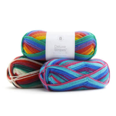 3 skeins of Universal Yarn Deluxe Stripes yarn. One in rainbow colors, one in maroon, pine, and cream, and one in light blue, dark blue, and red.