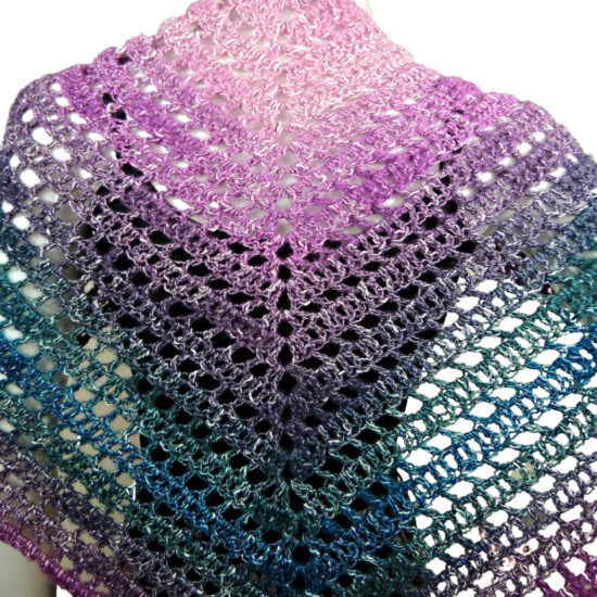 Close up of the back of a white mannequin in a black tank top, and a triangular crochet shawl that changes colors through pink, purple, green, and blue. Shawl alternates between rows of solid stitches and rows of net or eyehole stitches. The shawl is laying flat across the back so the stitching can clearly be seen.