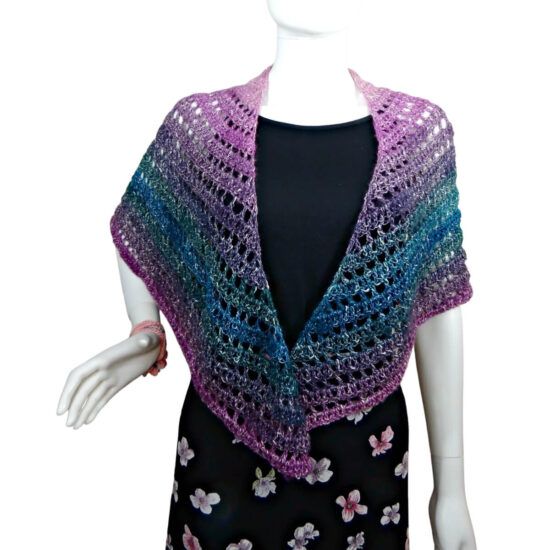 A white mannequin in a black tank top, black skirt and a triangular crochet shawl that changes colors through pink, purple, green, and blue. Shawl alternates between rows of solid stitches and rows of net or eyehole stitches. The point of the shawl is in back and the sides are over the shoulders, hanging in front.