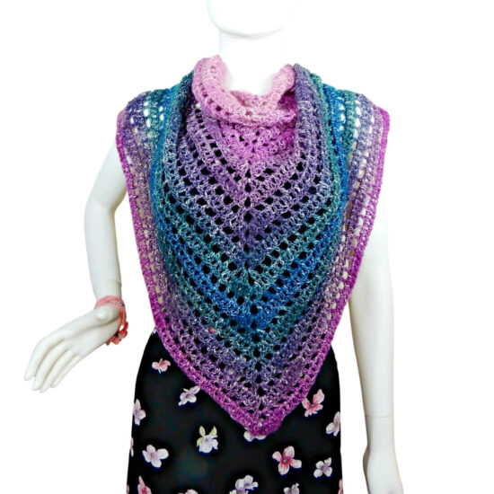 A white mannequin in a black tank top, black skirt and a triangular crochet shawl that changes colors through pink, purple, green, and blue. Shawl alternates between rows of solid stitches and rows of net or eyehole stitches. The point of the shawl is in front and the sides are pulled up around the shoulders.