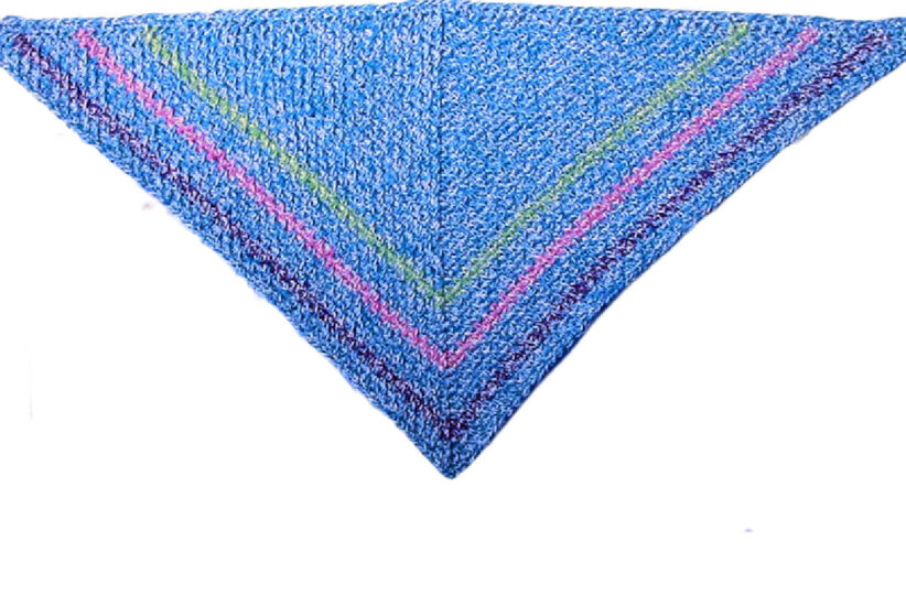 Flat lay overhead view of a crochet right angle 45/45/90 triangle. The triangle is light blue with 3 stripes close to the edge in green, pink, and purple.
