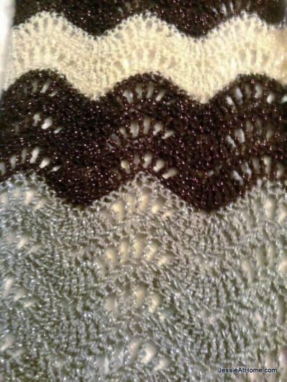 Rectangle image of a lacy crochet ripple stitch in stripes of black, white, and gray.