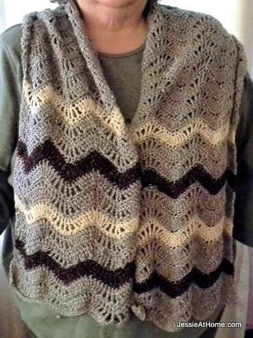 Close up of a person's torso wearing a rectangular shawl made of a lacy crochet ripple stitch in stripes of black, white, and gray.