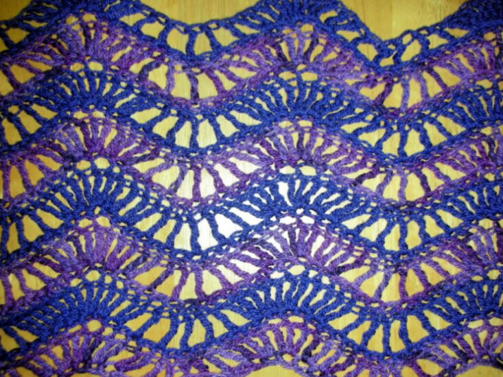 Close up of a rectangle of lacy crochet ripple stitches in stripes of medium and dark purple