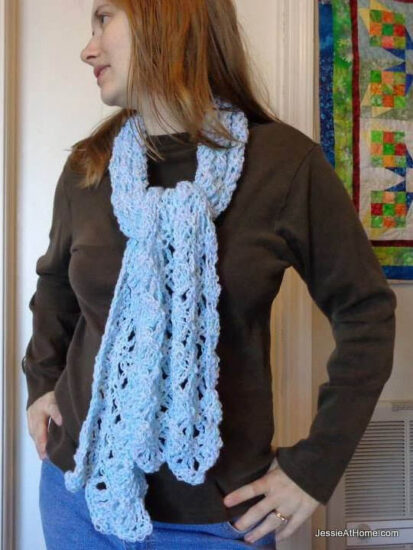 Waist up image of a woman in a brown top with wrap made of lacy crochet ripple stitches in light blue.