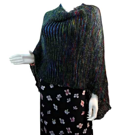White mannequin wearing a black tank and skirt and a knit poncho in black with bits of dark red, blue, and green. The poncho is waist length and straight across the front with a point hanging towards the back.