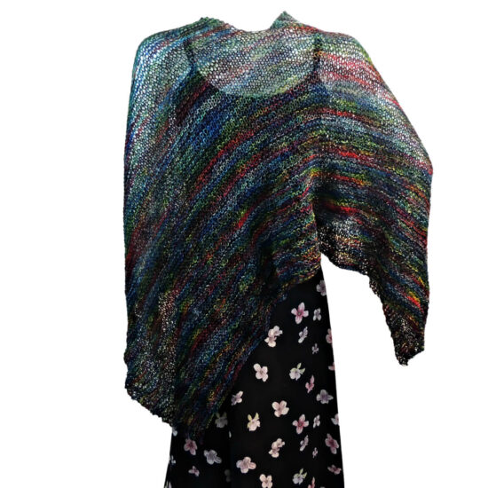 Back view of a white mannequin wearing a black tank and skirt and a knit poncho in black with bits of dark red, blue, and green. The poncho is waist length and straight across the front with points on the sides.