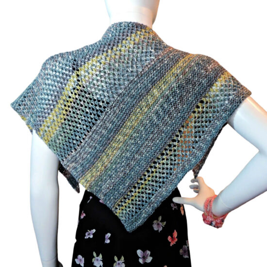 Back of a white mannequin wearing a black tank and skirt and a small triangular knit shawl. The shawl is knit in tweed yarn with long stripes of blue-gray and short stripes of yellow. The knitted fabric alternates between sections of garter stitch and a mesh stitch. The shawl lays flat against the back so the fabric can be clearly seen.