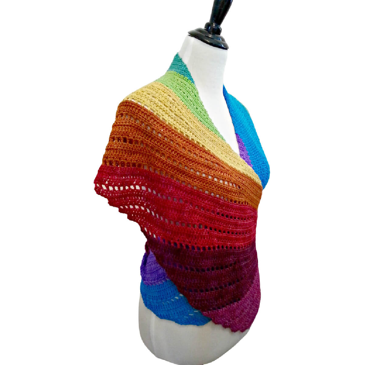 Front side view of a dress form torso. Wrapped around its shoulders then behind its back in a way that resembles a top is a curved long crochet wrap or shawl resembling a bird wing in rainbow colors starting with purple and ending with blue.