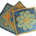 Image of 3 crochet granny squares, each with a single crochet border and an overlayed large flower with 8 petals each outlined in slip stitches. The squares are laying fanned out. They are each in combinations of yellow, blue and green.