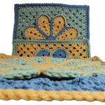 Image of 3 crochet granny squares, each with a single crochet border and an overlayed large flower with 8 petals each outlined in slip stitches. One is laying flat and the photo is taken across that one with 2 more behind each. They are each in combinations of yellow, blue and green.