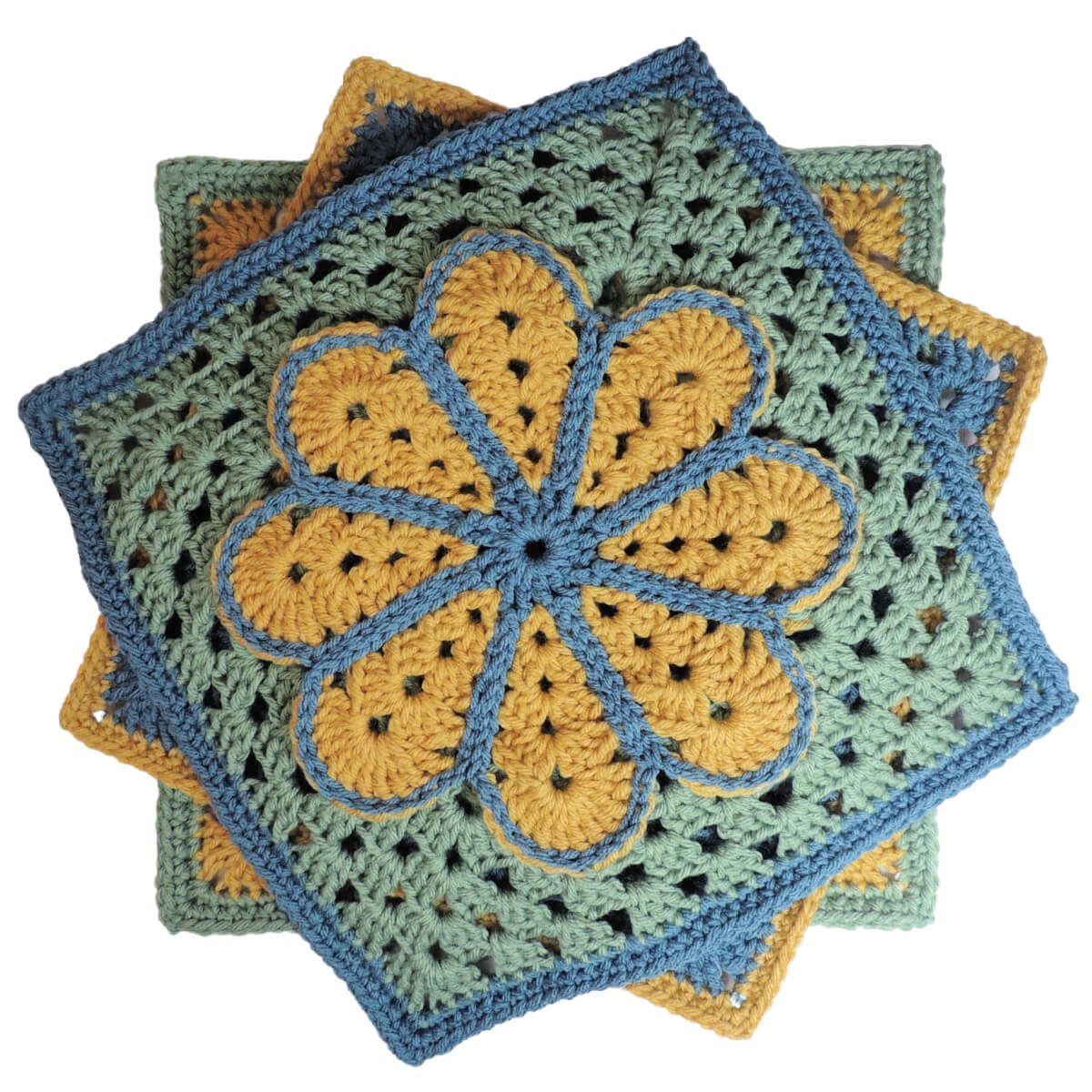 A crochet granny square with a single crochet border, overlayed on the square is a large flower with 8 petals each outlined in slip stitches. The square is yellow with a green border and the flower is blue with a green outline.