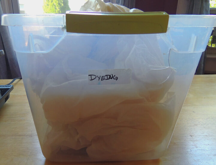 A clear plastic tub labeled "dyeing" filled with fabric.