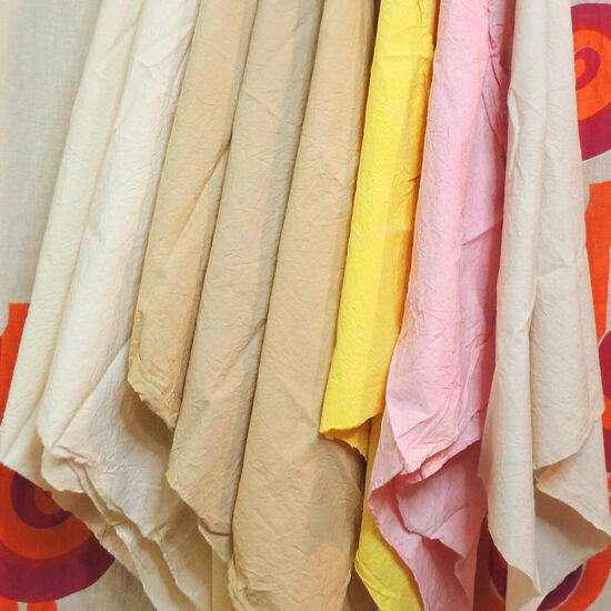 8 muslin pieces in various colors hanging in a row. The colors are: just a bit darker than muslin color, muslin color, tan, medium tan, slightly darker tan, yellow, pink, and very pale blue-gray.