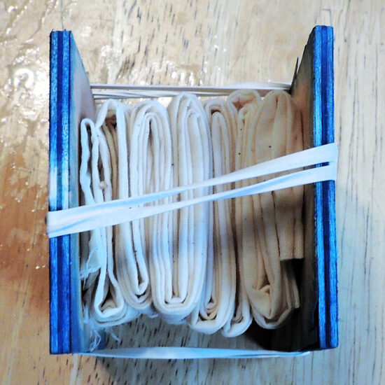 A piece of muslin fabric accordion folded two ways held between two pieces of wood. Rubber band hold the whole thing together.